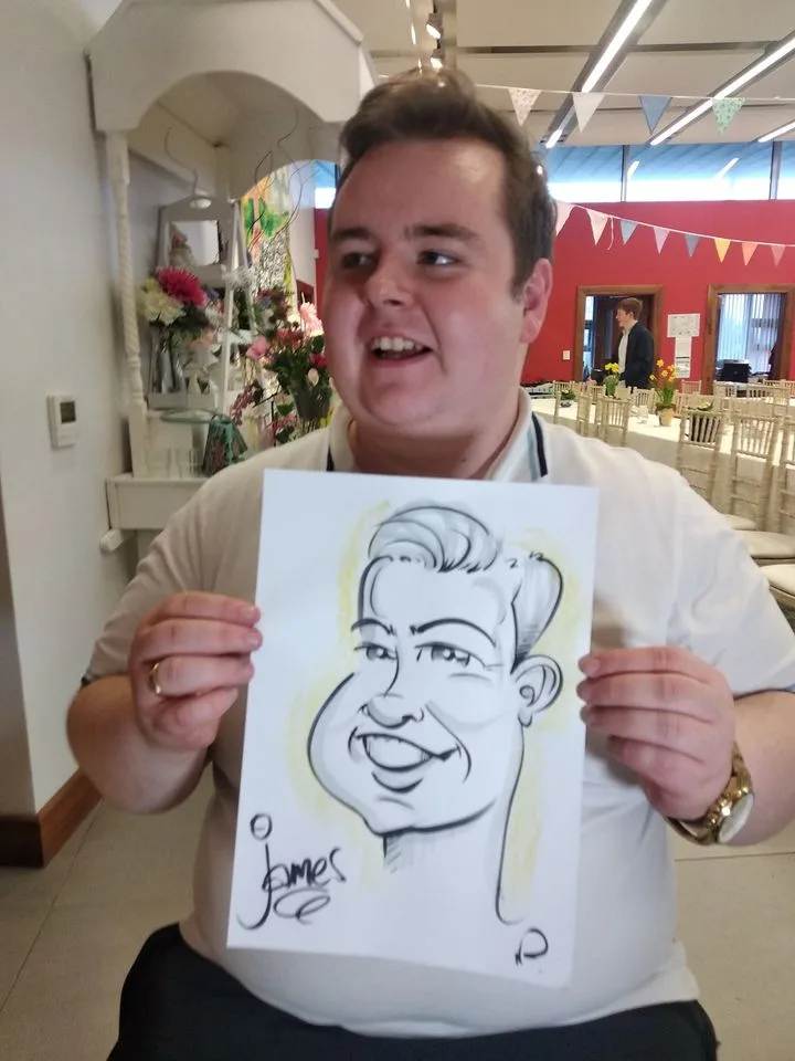 A young man holding up a caricature drawing